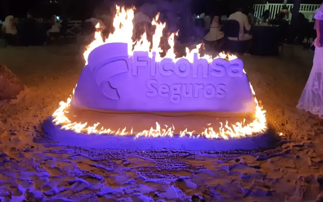 Sand sculpture of a company logo lit with fire at night, by Ronis Villeda in Roatan