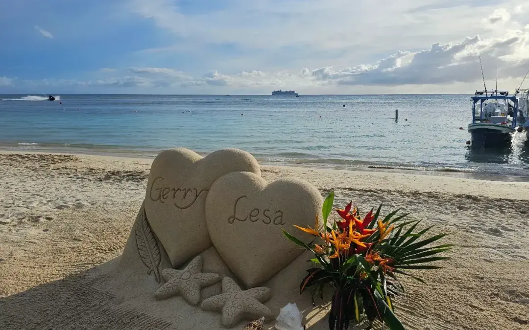 Two hearts with names and tropical flowers, sand sculpture on a Roatan beach